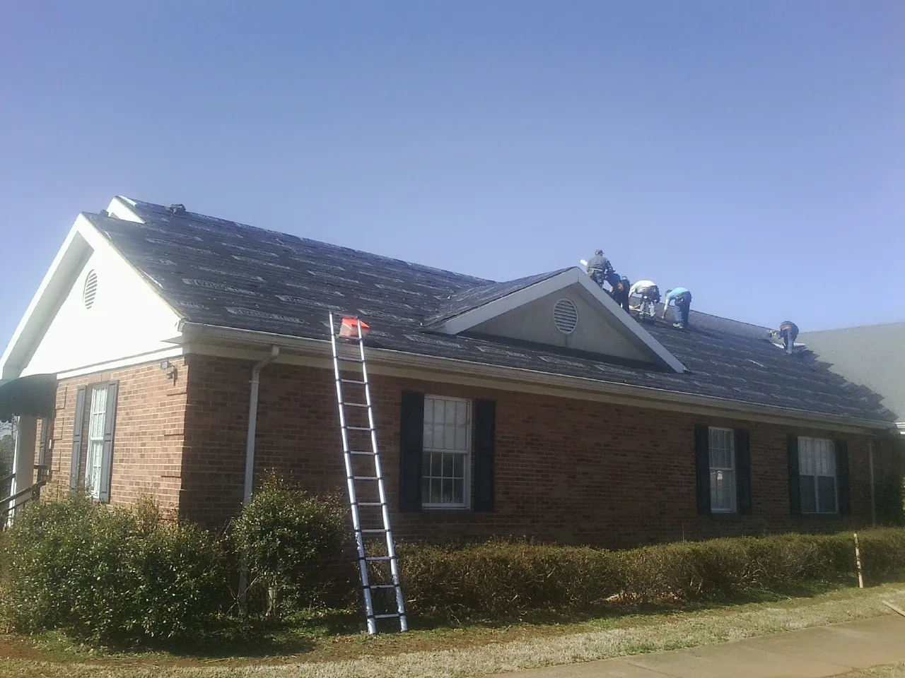 Crew tearing shingles off a brick ranch roof with a ladder set — Metal Roof Repair work by our crew in Saint Benedict