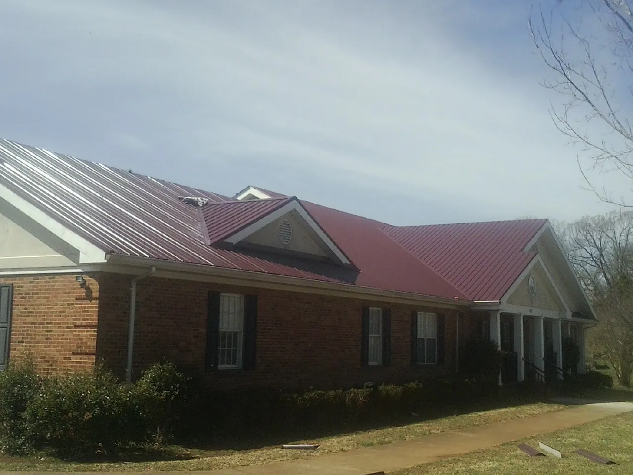 Red metal roof with gabled entries on a long brick building, from a Hail Damage Roof Repair job in Saint Benedict