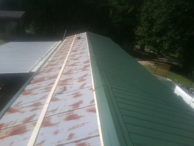 Old rusted panels beside newly installed green metal roofing — Wind Damage Roof Repair by Roofing Brothers in Saint Benedict
